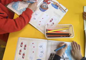Dzieci pracują z książkami przy stolikach, wykonują zadania, kolorują znak drogowy - przejście dla pieszych